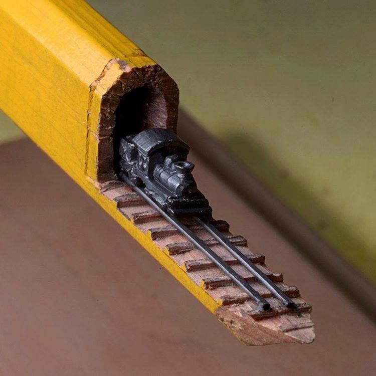 A train coming out of a tunnell on its track carved in a pencil.